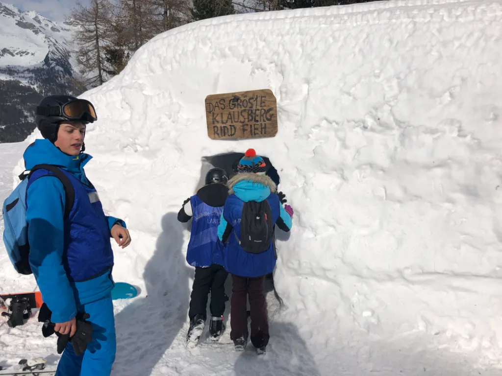 Jugendliche gehen durch einen Schneetunnel mit Holzschild.